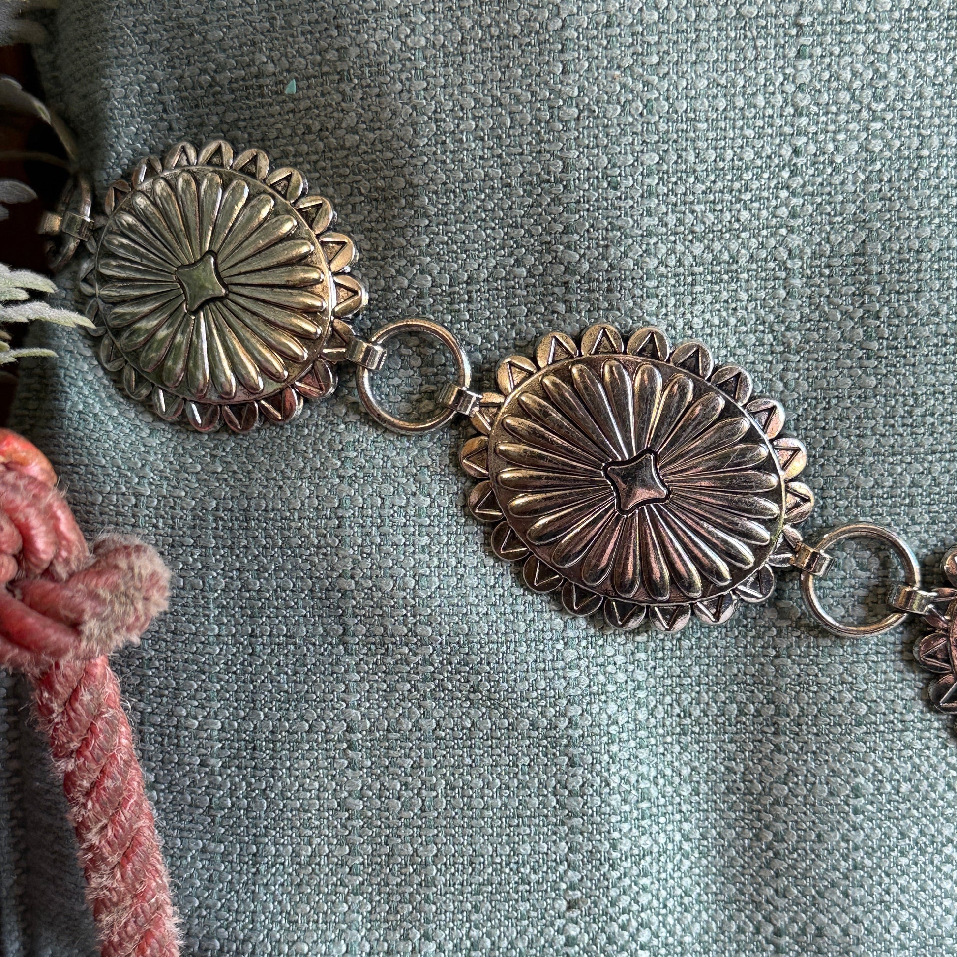 Close-up view of Western concho belt with antiqued silver tone oval scalloped conchos and a raised sunburst pattern.